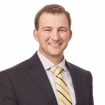 A man in a suit and yellow tie smiles