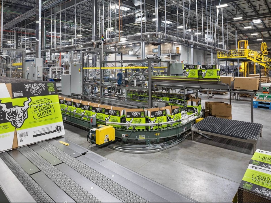 Many conveyer belts assemble and move green boxes inside a gray warehouse.