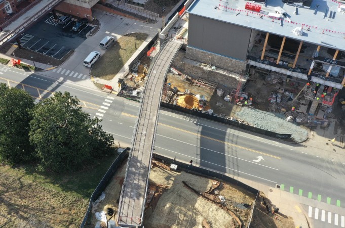 A bridge is constructed over a road, connecting a construction site to a large hill.