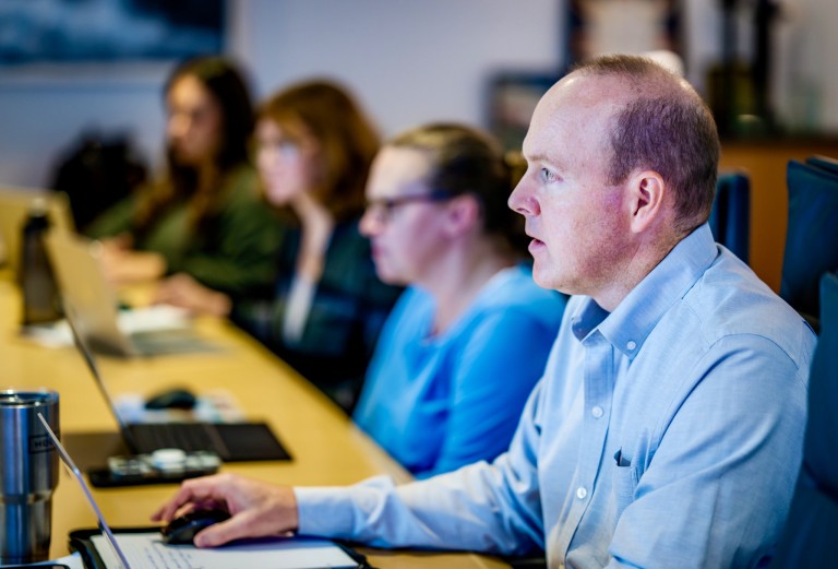 A man sits at a conference table and works on a laptop.