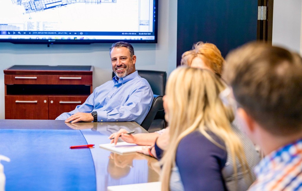 a man sits at the end of a conference table and smiles.