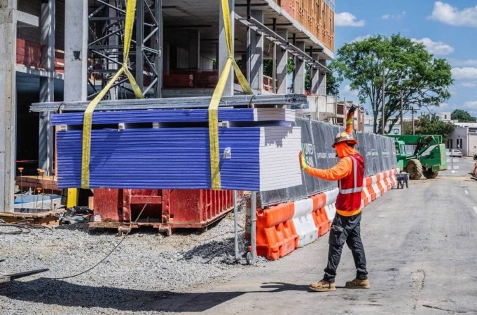A man in construction safety equipment stands next to a pile of material being moved by a crane.
