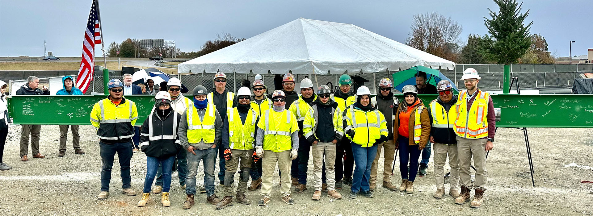 Trade partner group in safety gear standing in front of steel beam with signatures
