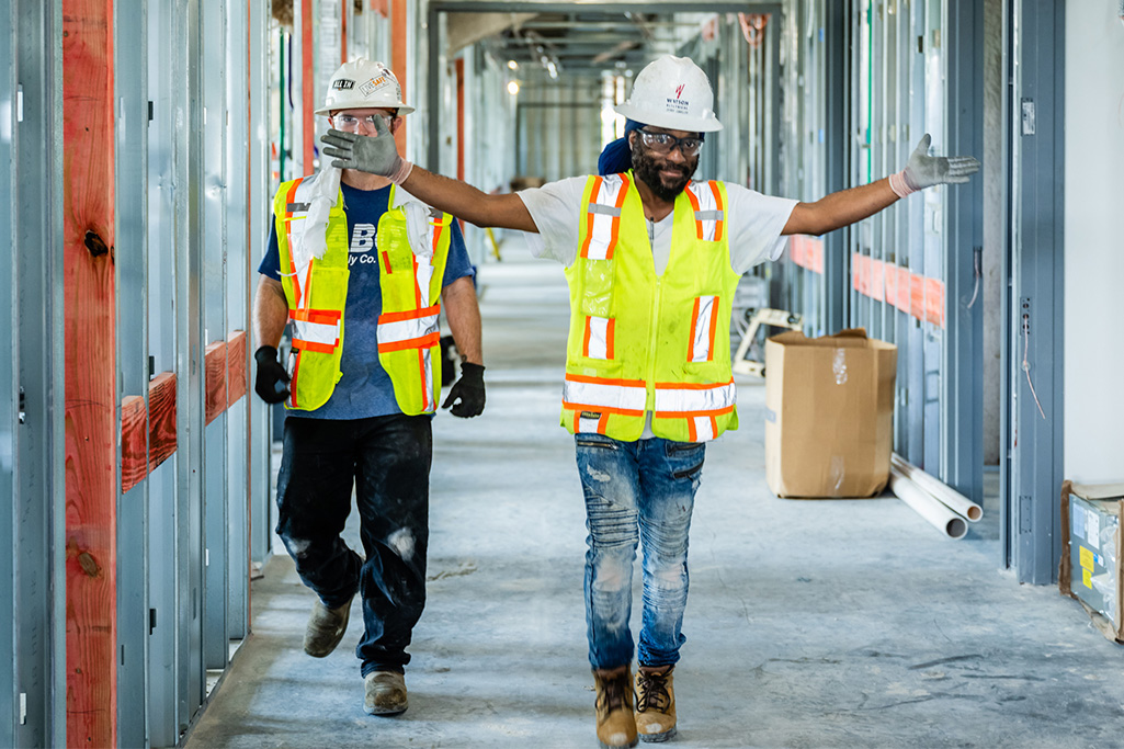 two men in safety gear walking down hallway of construction site
